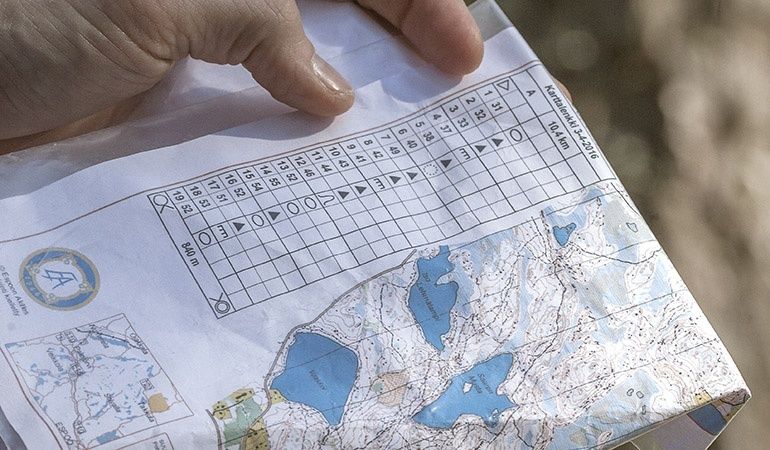 Hand håller en orienteringskarta med kontrollbeskrivningar och IOF-symboler