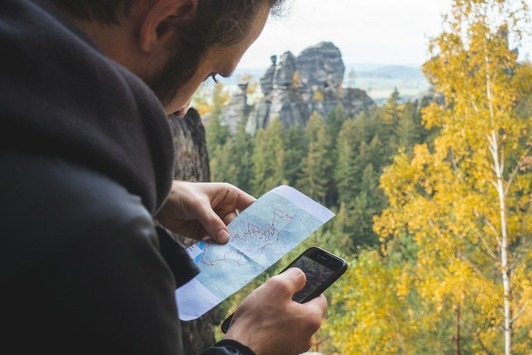 Person jämför en karta med mobilen vid en skogklädd bergsterräng